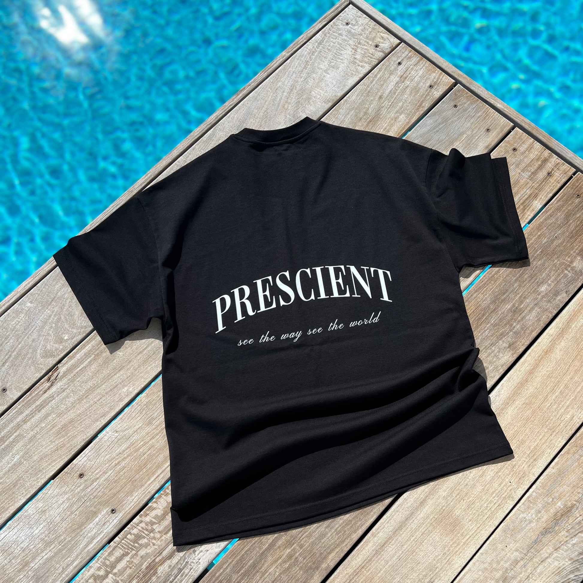 Prescient Classic Black T-Shirt laying on decking beside a pool